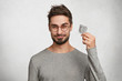 © wayhome.studio  - Curious bearded male holds new kind of condom, wonders about its quality, wears casual grey sweater, stands against white concrete wall. Handsome young man advertises product of contraception
