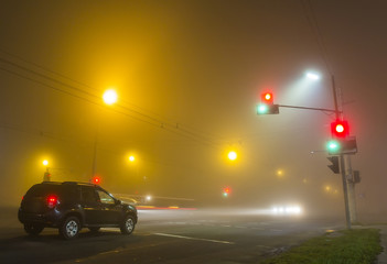 Canvas Print - Thick fog over empty road with lonely car and traffic lights at night