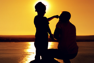 Wall Mural - Rear view - young unknown father holding small son in hat by the hand and looking at the beautiful view of the sea against the backdrop of customary bright sun.