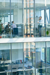 Wide angle portrait of mature businessman speaking by phone standing behind floor to ceiling windows in modern office building, copy space