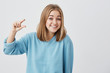 © Cookie Studio - Young attractive woman wearing blue sweater showing something little with hands while gesturing and broadly cmiling. Blonde female student demonstrating size of something against gray studio wall