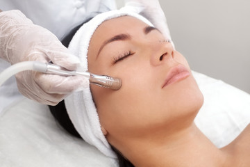 The cosmetologist makes the procedure Microdermabrasion of the facial skin of a beautiful, young woman in a beauty salon.Cosmetology and professional skin care.