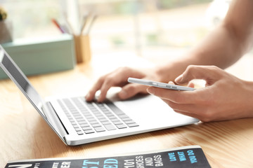 Wall Mural - Man using cell phone and laptop on table, closeup