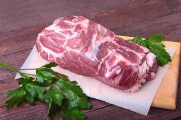 Raw pork neck chop meat with parsley herb leaves on a stone background. Ready for cooking.