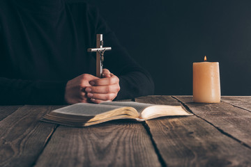 cropped image of christian sitting with cross in hands