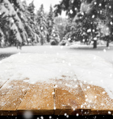 Wall Mural - Wooden desk covered by snow and snowy park on background