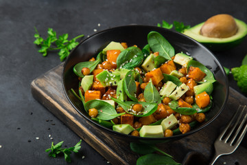  Avocado, quinoa, roasted sweet potato, spinach and chickpeas salad in black bowl.