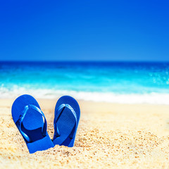 Summer holiday beach background with flip flops on a tropical beach. Slippers from a sand on a beach, funny concept .