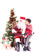 © Mediaphotos - Santa Claus sitting in chair near Christmas tree with multi-ethnic boy and girl on his lap