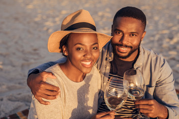 Smiling African couple sitting together at the beach drinking wine 