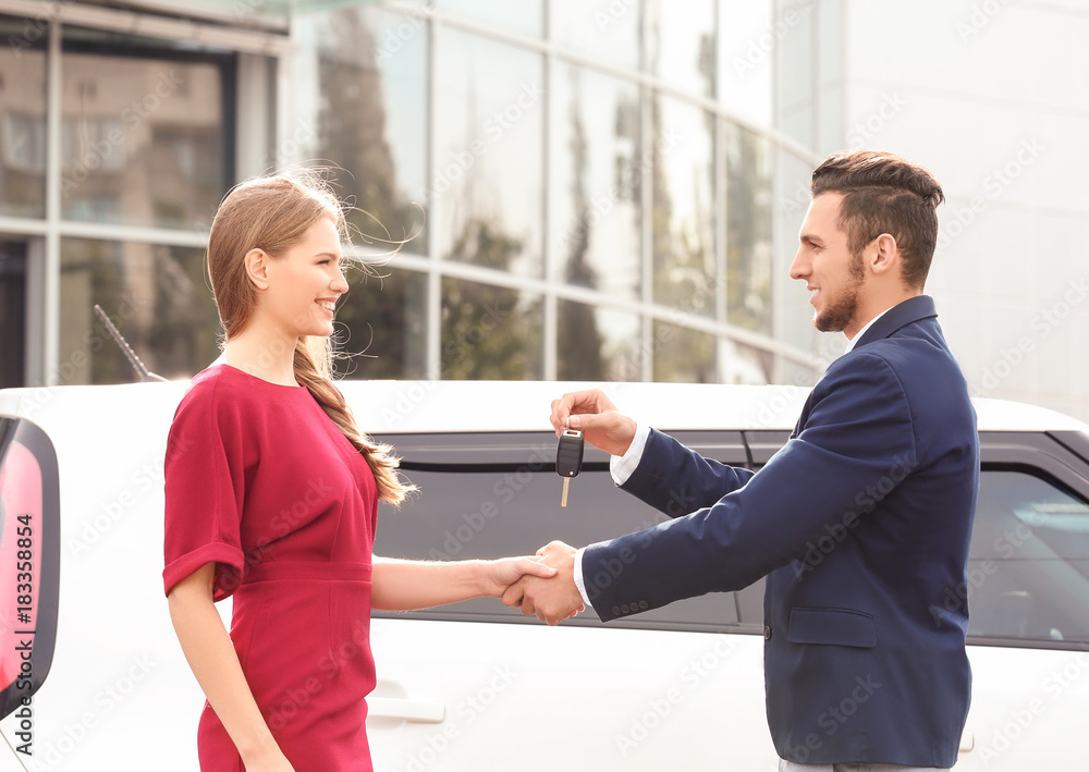 Salesman giving car key to customer outdoors