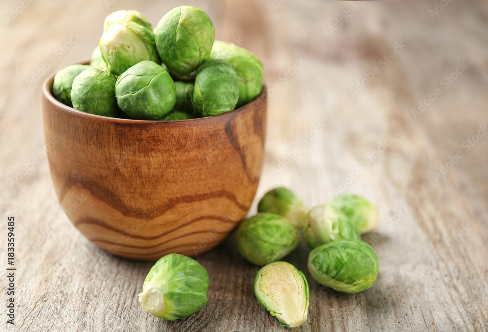 Bowl with raw Brussels sprouts on wooden background