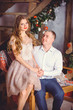 © T.Den_Team - New year holiday portrait of a man and woman surprising him with a Christmas gift. Couple celebrating Christmas together. Beautiful young couple is celebrating at cozy romantic place.