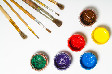 paints in jars and a brush on a white sheet of paper, top view