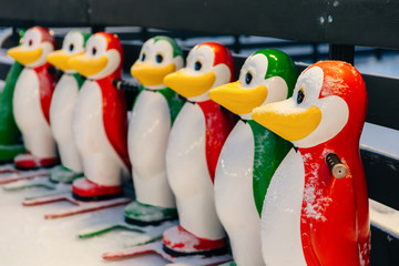 Horizontal shot of colorful skate aids in shape of funny penguins, needed to keep balance on ice rink, stand on ice covered with snow or skating arena