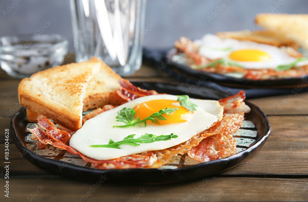 Plate with fried egg and bacon on wooden table