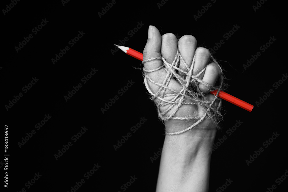 Hand with red pencil tied with rope, depicting the idea of freedom of the press or freedom of expression on dark background in low key. international human rights day concept. - obrazy, fototapety, plakaty 