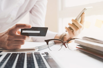 Close up hand of woman holding credit card and using smartphone at home. Online shopping concept