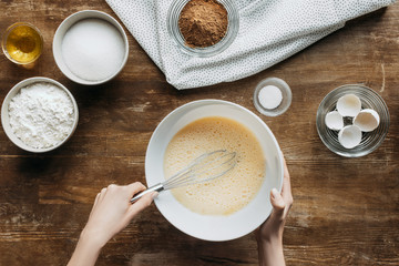 Wall Mural - cropped shot of woman whisking liquid for baking pancakes on wooden table