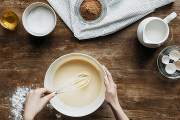 Wall Mural - cropped shot of woman whisking ingredients for baking pancakes on wooden table