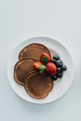 Wall Mural - top view of chocolate pancakes with berries on white table