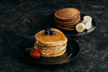 Wall Mural - plates with stacks of tasty pancakes with fruits on black table