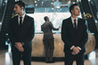 © LIGHTFIELD STUDIOS - two bodyguards waiting for businessman standing at reception counter