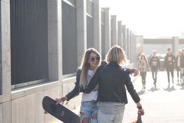 Two girl friends having fun together with skateboard. Outdoors, urban lifestyle.