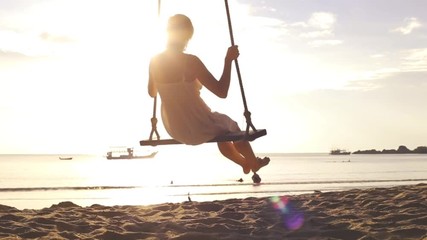 Wall Mural - Slow motion footage of happy woman on rope swing at the beach during vacation holidays and crossing the sun, travel destination leisure concept