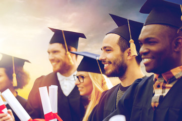 happy students in mortar boards with diplomas