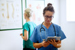 © dusanpetkovic1 - Focused professional middle aged nurse looking in a tablet in front of another nurse while looking on medical papers on the wall.