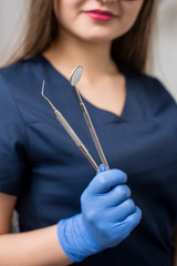 Wall Mural - Dentist with blue gloves holding tools - dental mirror and dental probe at the dental office. Close-up, selective focus on tools. Dentistry