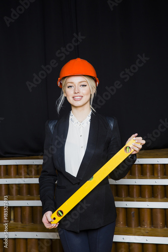 Cuadros en Lienzo Beautiful blonde businesswoman with application tier at loft office in orange construction helmet and suit