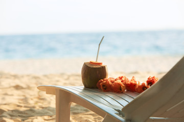 Coconut with drinking strawand lei flowers on beach bench or deck chair with blue ocean and white sand on background. Maldives