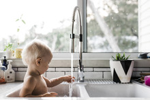 Side View Of Shirtless Toddler Playing With Water While Sitting In Kitchen Sink At Home