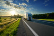 © am - White delivery truck driving on the asphalt road in rural landscape at sunset