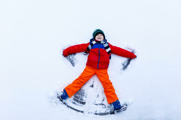 Poster - Cute little kid boy in colorful winter clothes making snow angel, laying down on snow