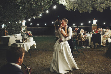 Groom hugs bride tender while they dance on the backyard in the evening