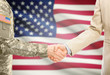 USA military man in uniform and civil man in suit shaking hands with adequate national flag on background - United States of America