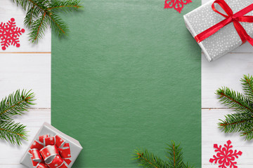 Christmas background with decorations on white wooden table and green tablecloth with free space for greeting text. Gifts, fir branches and snowflake decorations. Top view.