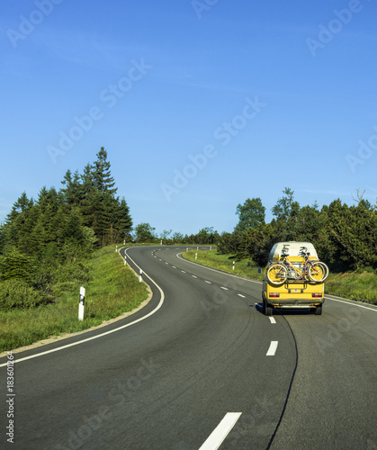 Plakat VW Camper van z rowerami na zakrętu wiejskiej drodze w regionie Schwarzwaldu