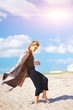 © raisondtre - Modern young beautiful girl in fashionable clothes enthusiastically dancing barefoot with eyes closed on sandy beach a Sunny day.