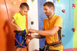 © Africa Studio - Father and son learning rock climbing safety, instructor teaching child how to tie a knot on climbing harness, an instructor guides a young boy in proper climbing equipment usage on an indoor