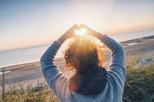 Girl holding a heart-shape with sunset light on the beach Billede på lærred