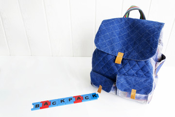 Blue bag with puzzle letters on white table. Hand made backpack for travelers.