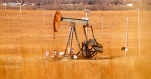 Rusty Gas - Oil Pumpjack In An Orange Winter Field Full Of Electric Poles With Blurred Grass In The Foreground