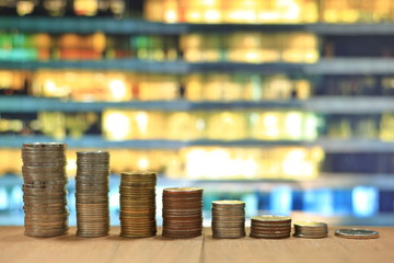 declining chart made of coin piles stacked tower on wooden board with blured hi-tech building in the background