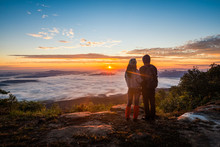 Young Couple Watching The Sun Rise From Top Of Mountain