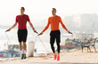 Handsome young men wearing sportswear and  skipping rope at quay during autumn