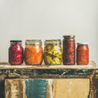 Autumn seasonal pickled or fermented vegetables in jars placed in line over vintage rustic kitchen drawer, white wall background, copy space, square crop. Fall home food preserving or canning
